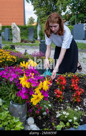 Jeune femme qui tend vers une tombe, au cimetière, Gelting, près de Wolfratshausen, haute-Bavière, Bavière, Allemagne, Europe Banque D'Images