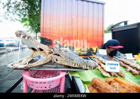 Une viande de crocodile, rue vendeur montre deux têtes de croc séchées, bouche agape, avec des dents tranchantes, à côté de divers kebabs et d'autres préparations de la viande, Banque D'Images
