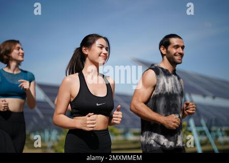 Active style de vie jeune homme coureur courir par panneaux solaires ferme à l'extérieur arrière-plan d'été. Concept de durabilité Banque D'Images