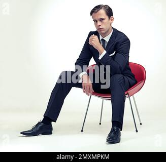 Confiante tout.Un portrait studio d'un jeune gentleman beau dans un costume à fines rayures assis sur une chaise. Banque D'Images