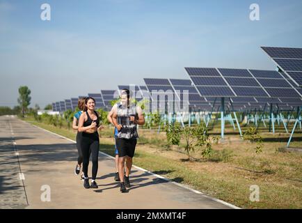 Active style de vie jeune homme coureur courir par panneaux solaires ferme à l'extérieur arrière-plan d'été. Concept de durabilité Banque D'Images