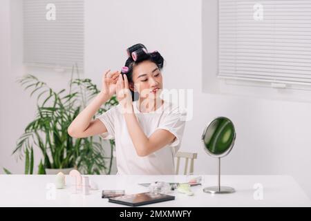 Belle jeune femme adulte dans le rouleau de cheveux regardant dans le miroir Banque D'Images