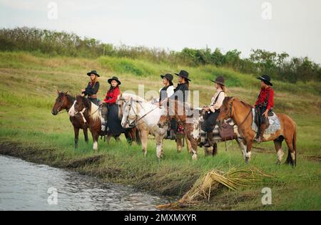 cowboy sur son cheval pendant la course des chevaux et, en arrière-plan, un groupe de six cowboys et cowgirls supervisant la course des chevaux Banque D'Images