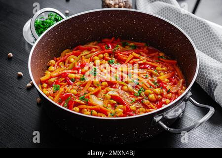 Ragoût de légumes de pois chiches, carottes, poivrons doux, oignons, ail et sauce tomate avec citron sur la table sombre. Cuisine orientale. Banque D'Images