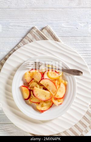 rondelles d'oignon frit et de pomme rouge sur plaque blanche avec fourchette sur table en bois blanc, vue verticale Banque D'Images