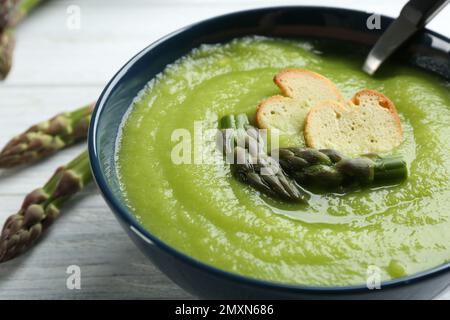 Délicieuse soupe d'asperges dans un bol sur une table en bois blanc, en gros plan Banque D'Images