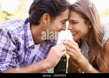 Nature, heureux et couple partageant un verre avec amour lors d'un pique-nique d'été dans un jardin extérieur. Bonheur, sourire et jeune homme et femme buvant un Banque D'Images