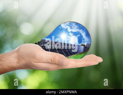 Source d'énergie alternative. Homme tenant une ampoule avec panneaux solaires, gros plan Banque D'Images
