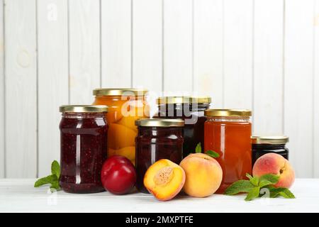 Pots en verre avec différents fruits marinés et confitures sur fond de bois blanc Banque D'Images