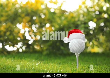 Balle de golf avec petit chapeau de père Noël sur le tee-shirt sur fond flou. Espace pour le texte Banque D'Images