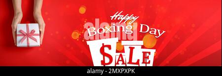 Motif banderole de solde le lendemain de Noël. Femme tenant un cadeau sur fond rouge, gros plan Banque D'Images