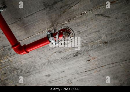 Un détail d'un plafond rustique avec des tuyaux rouges et une alarme incendie Banque D'Images