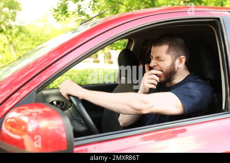 Un homme fatigué bâilling en conduisant sa voiture moderne Banque D'Images