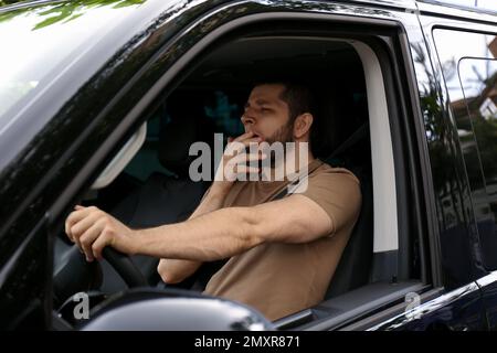 Un homme fatigué bâilling en conduisant sa voiture moderne Banque D'Images