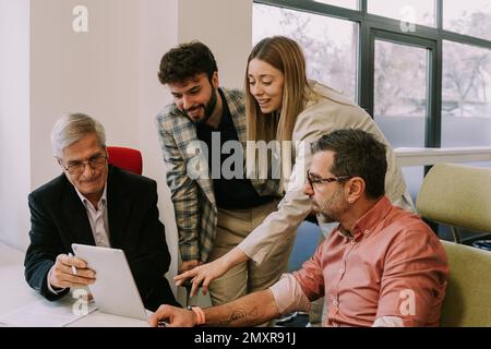 Deux collègues principaux tentent de résoudre le problème du projet. Leurs collègues juniors plaisantent avec eux Banque D'Images