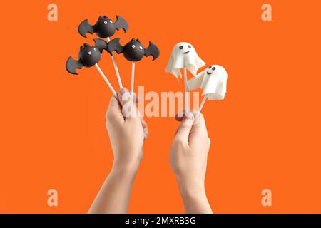 Femme avec un délicieux fantôme et un gâteau en forme de chauve-souris apparaît sur fond orange, gros plan. Fête d'Halloween Banque D'Images