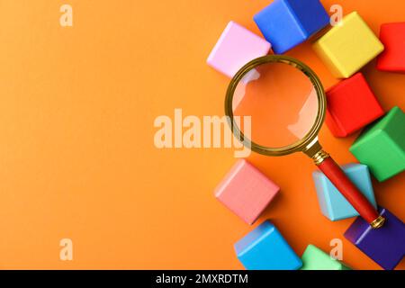 Différents cubes colorés et loupe sur fond orange, plat avec espace pour le texte. Concept de mots-clés de recherche Banque D'Images