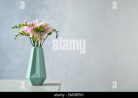 Superbes freesias en fleurs dans un vase sur une table sur fond bleu. Espace pour le texte Banque D'Images