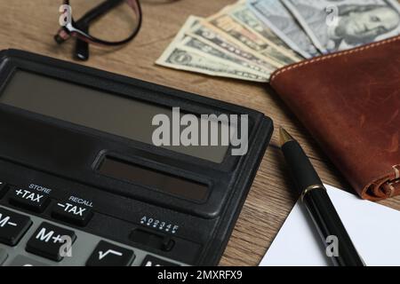 Calculatrice, stylo et portefeuille avec argent sur table en bois, gros plan. Comptabilité fiscale Banque D'Images