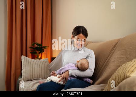 Mère heureuse prenant soin de son petit bébé dormant dans ses bras à la maison - concept de famille et de maternité Banque D'Images