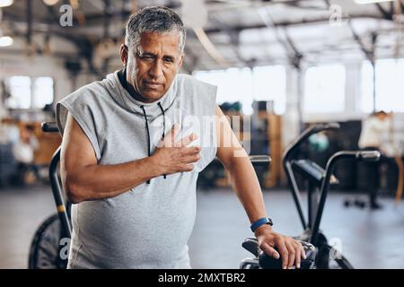 Gym, douleur à la poitrine et homme âgé avec urgence médicale pendant l'entraînement sportif au studio de fitness. Santé, bien-être et inflammation, vieil homme à la main Banque D'Images