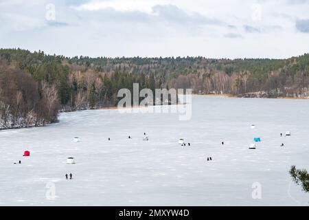 Pêcheurs pêchant sur un lac gelé en hiver avec un poteau ou une canne de pêche, une tarière de glace, divers équipements pour la pêche et des tentes thermiques portables, aériennes Banque D'Images