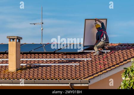 Un installateur photovoltaïque installe un panneau solaire sur un toit carrelé rouge Banque D'Images