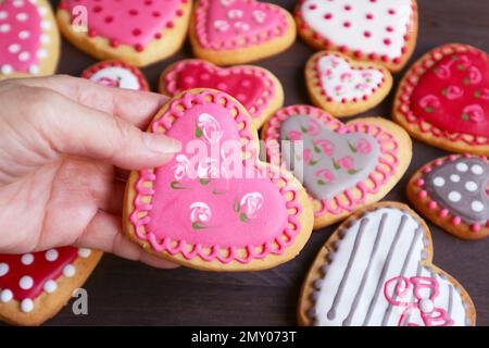 Vous cueillir à la main des biscuits glaçages royaux en forme de cœur avec un tas de biscuits en arrière-plan Banque D'Images