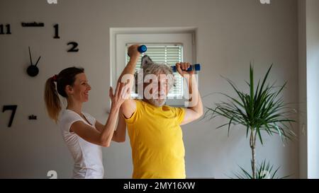 Une jeune femme physiothérapeute travaillant avec un homme âgé gai l'enseignant à l'exercice avec des haltères. Image conceptuelle de la vie active d'une pensione Banque D'Images