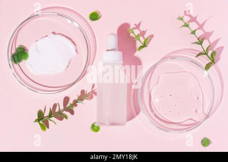 Pot à cosmétiques avec bouchon blanc et pipette sur fond rose. Boîtes de Petri avec gel et crème sur fond rose. Entouré de plantes. Banque D'Images