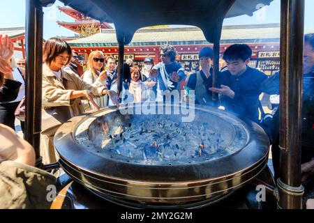 Tokyo, le célèbre sanctuaire d'Asakusa et temple Sensoji. Close up, les gens autour du grand brûleur en agitant la fumée au-dessus d'eux-mêmes. Banque D'Images