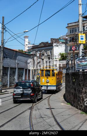 Un tramway de Santa Teresa qui retourne dans le quartier Centro tout en étant suivi d'une voiture dans la rue Almirante Alexandrino sous le ciel bleu de l'après-midi d'été. Banque D'Images