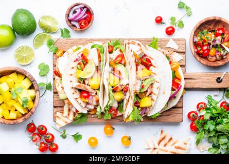 Tacos au poulet grillé, sauce à la sauce tomate, mangue, coriandre et oignon dans la tortilla sur la planche à découper. Arrière-plan de table blanc, vue du dessus Banque D'Images