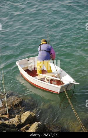 Un homme en équipement de pluie pêchant sur un petit bateau de pêche. Banque D'Images