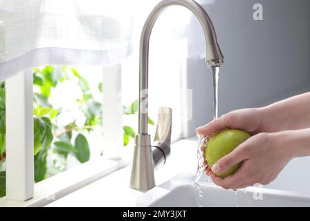 Femme lavant la pomme sur l'évier dans la cuisine, gros plan. Espace pour le texte Banque D'Images