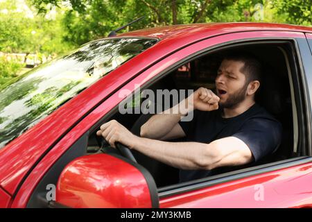 Un homme fatigué bâilling en conduisant sa voiture moderne Banque D'Images