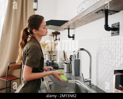 Femme fatiguée et fâchée mains sans gants lave la vaisselle avec une éponge de lave-vaisselle avec des bulles, des tâches ménagères, pas de lave-vaisselle, de l'eau élevée Banque D'Images