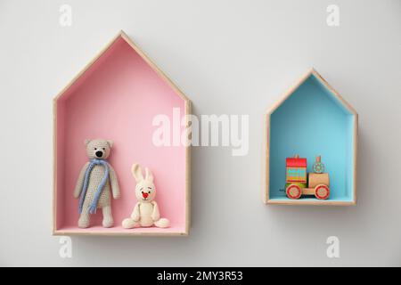 Étagères élégantes en forme de maison avec jouets sur un mur blanc. Décoration intérieure de la chambre de bébé Banque D'Images