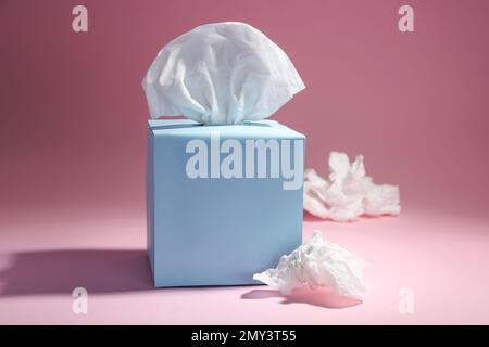 Boîte de mouchoirs en papier et serviettes de table froissés sur fond rose Banque D'Images