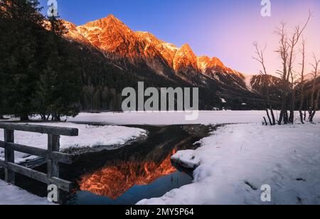 Les montagnes enneigées des Alpes reflètent les couleurs chaudes du lac Anterselva partiellement gelé au coucher du soleil en hiver. Neige et glace au premier plan Banque D'Images