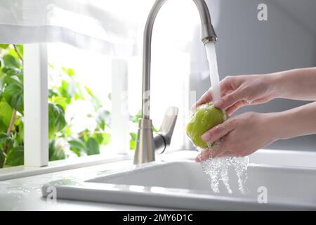 Femme lavant la pomme sur l'évier dans la cuisine, gros plan. Espace pour le texte Banque D'Images