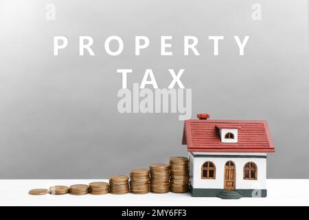 Texte taxe sur la propriété près des pièces empilées et modèle de maison sur fond gris Banque D'Images