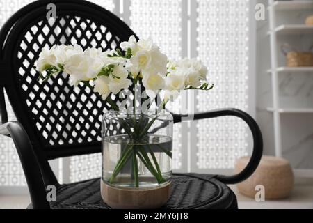 De belles fleurs de freesia blanches dans un vase sur un fauteuil à l'intérieur Banque D'Images