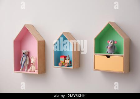 Étagères élégantes en forme de maison avec jouets sur un mur blanc. Décoration intérieure de la chambre de bébé Banque D'Images