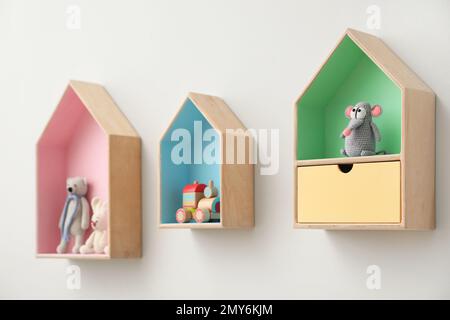 Étagères élégantes en forme de maison avec jouets sur un mur blanc. Décoration intérieure de la chambre de bébé Banque D'Images