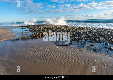 Les vagues de l'océan Atlantique s'écraseront sur les rochers de corail exposés à marée basse à Palm Beach en Floride. Banque D'Images