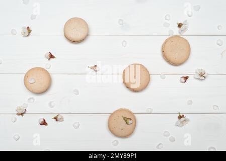 Biscuits macareux beige sur fond de bois blanc. Fleurs printanières d'abricot. Mise en page à plat, vue de dessus Banque D'Images