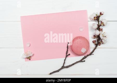 Biscuits d'amande rose et une branche avec les fleurs d'abricot. Feuille de papier pour notes sur fond blanc en bois. Modèle pour la conception. Plat la Banque D'Images