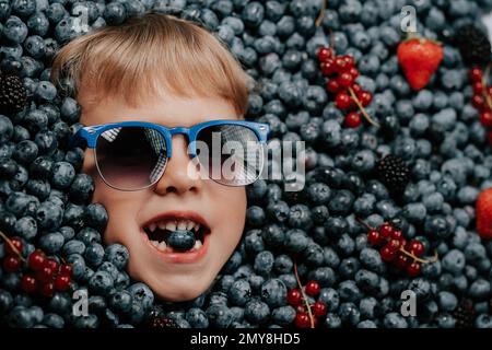 Visage de petit garçon souriant dans des baies mûres bleuets, plante de myrtille biologique Banque D'Images