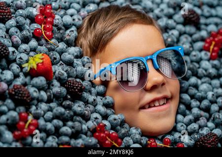 Visage de petit garçon souriant dans des baies mûres bleuets, plante de myrtille biologique Banque D'Images